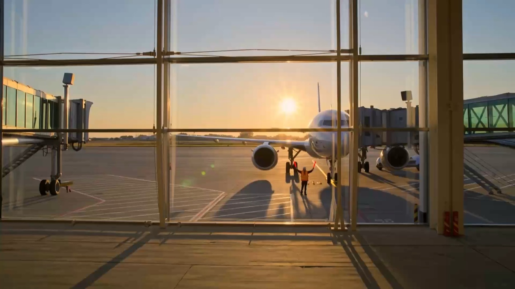 Ground crew member guiding an airliner to the gate at sunrise