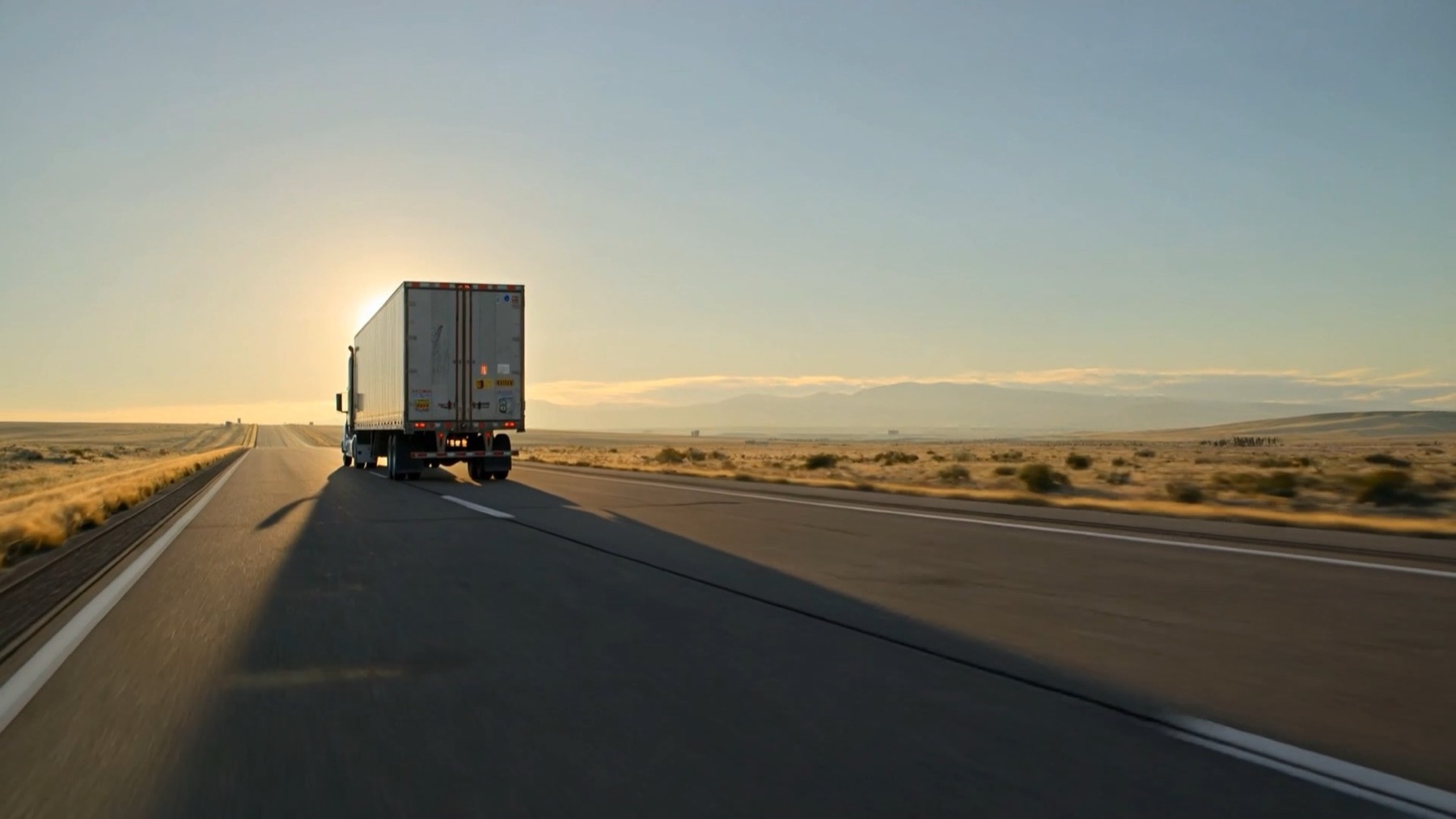 Semi truck driving down an open highway at sunrise
